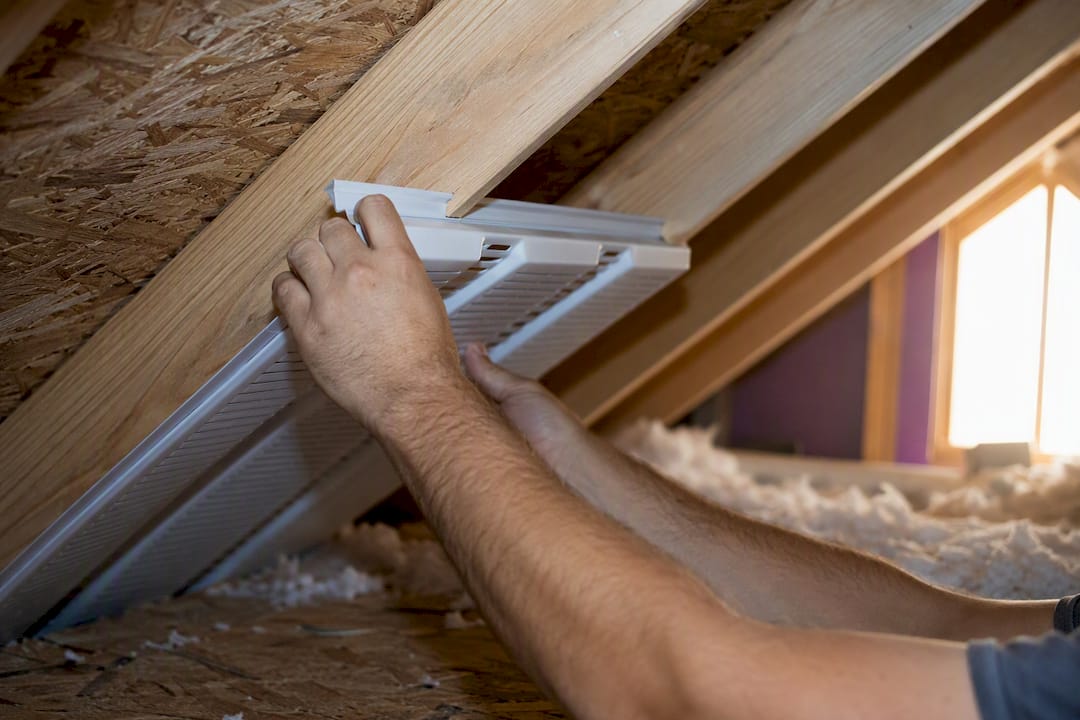 Hands installing rafter baffles in attic